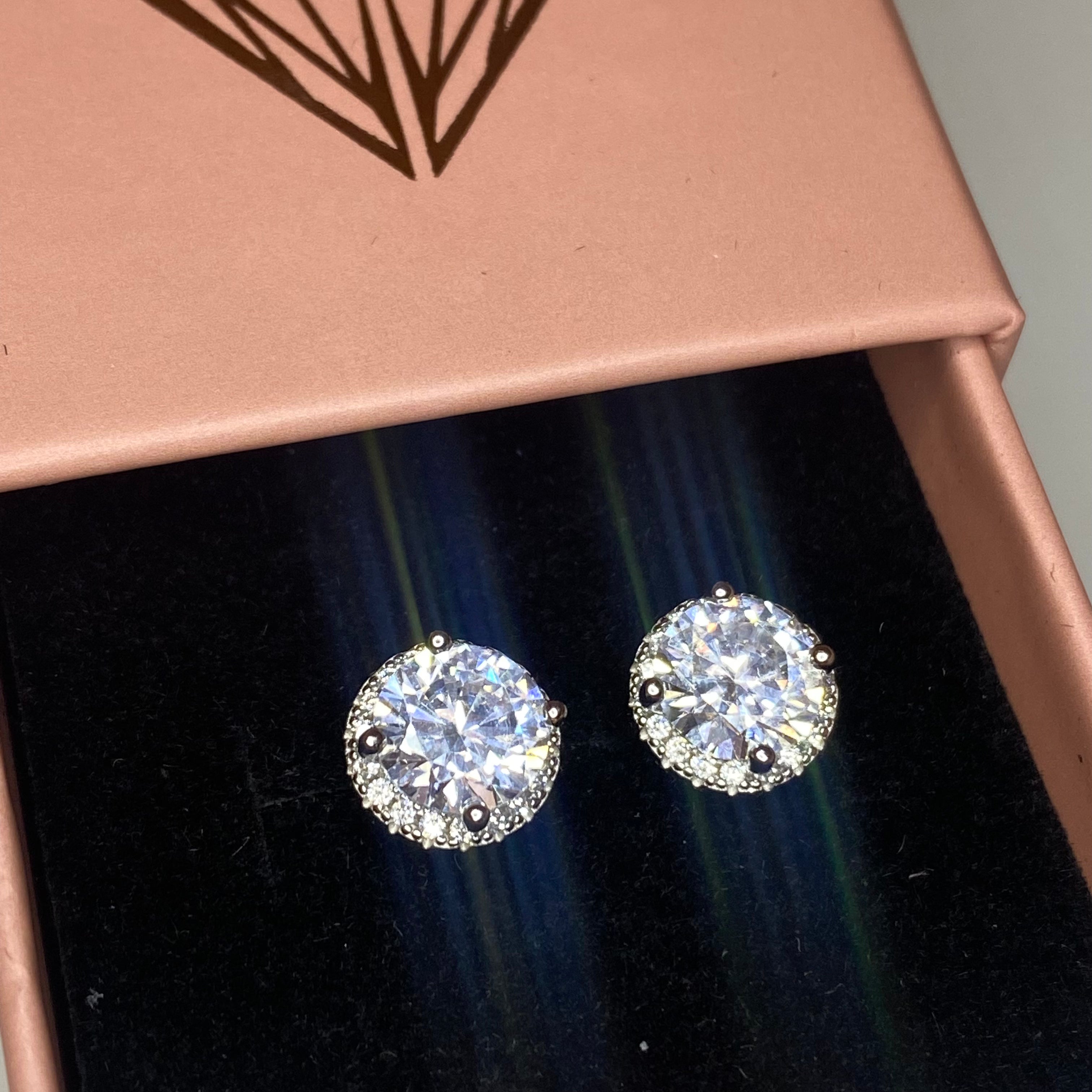 A pair of rhodium-plated stud earrings with a clear, zirconia main stone set in a small circle design.