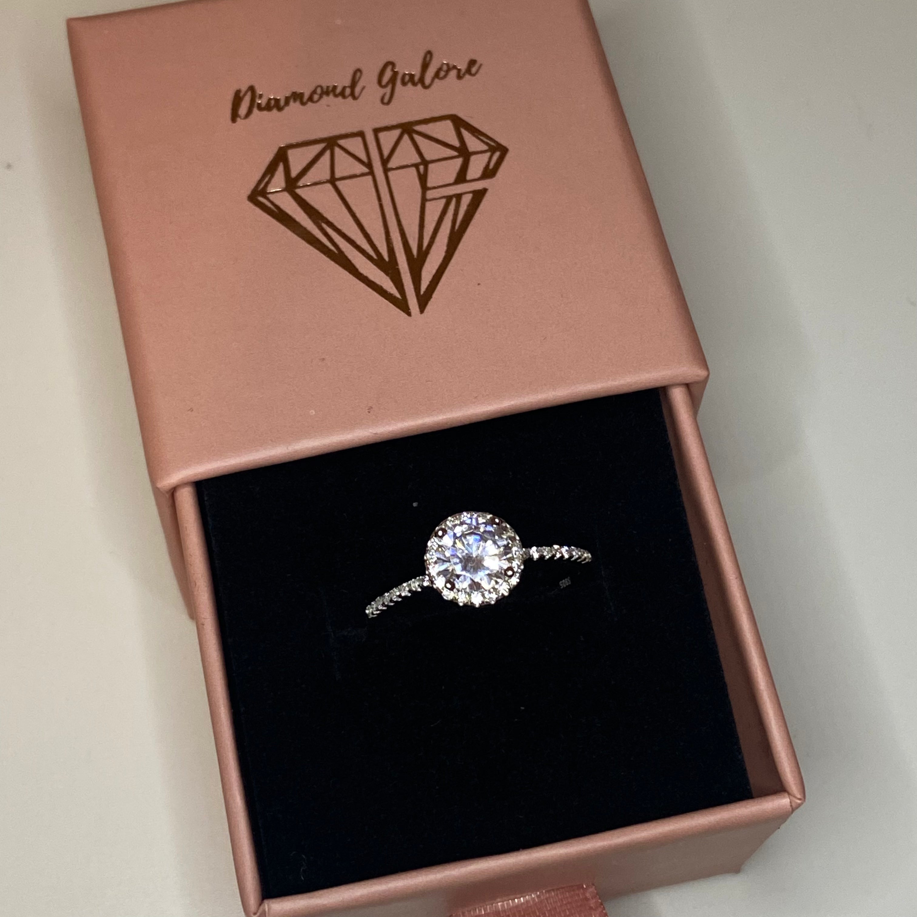 A sterling silver engagement ring with a central cubic zirconia stone surrounded by smaller clear stones, featuring a classic six-prong setting.