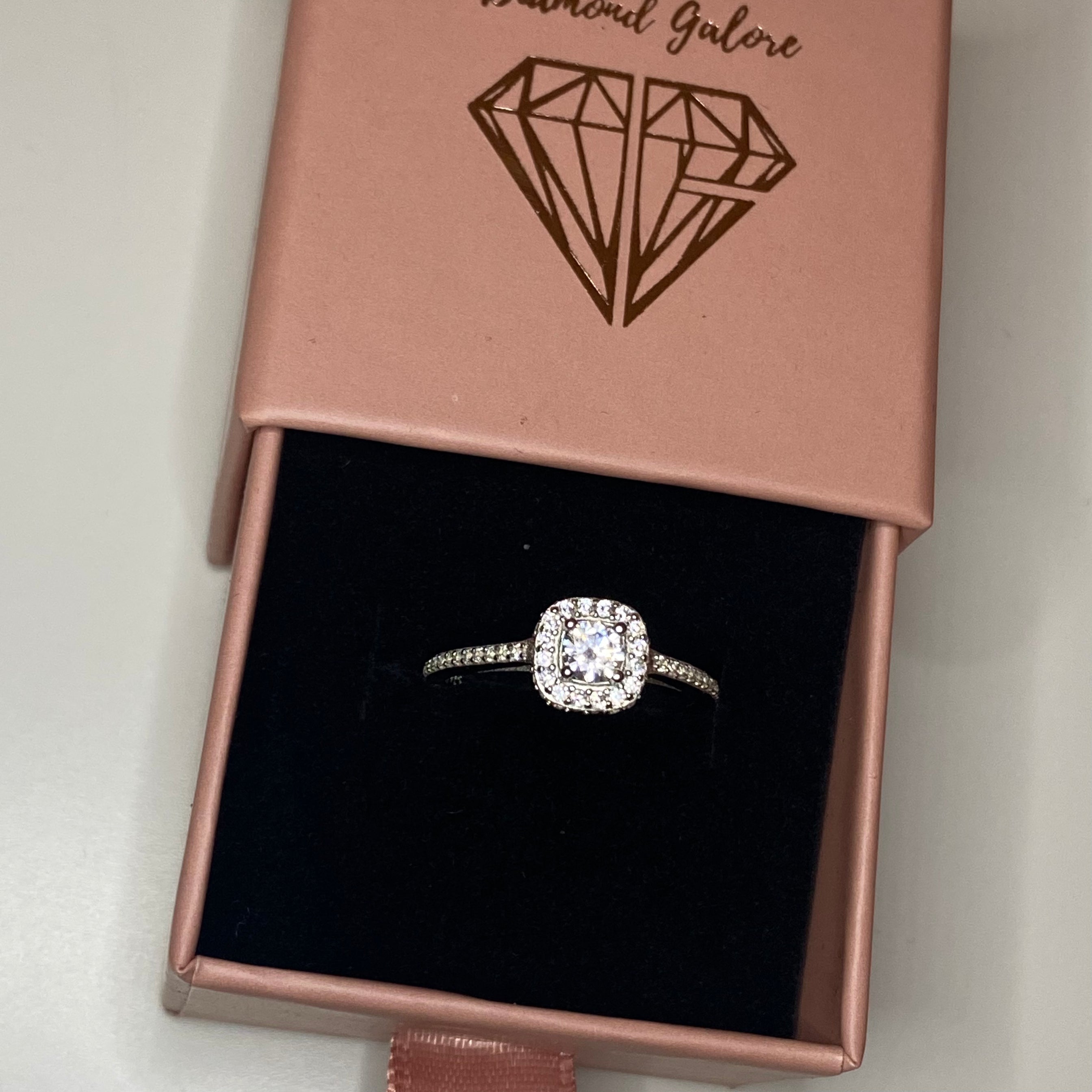 A silver square ring with a central cubic zirconia and surrounded by smaller clear stones on the band.