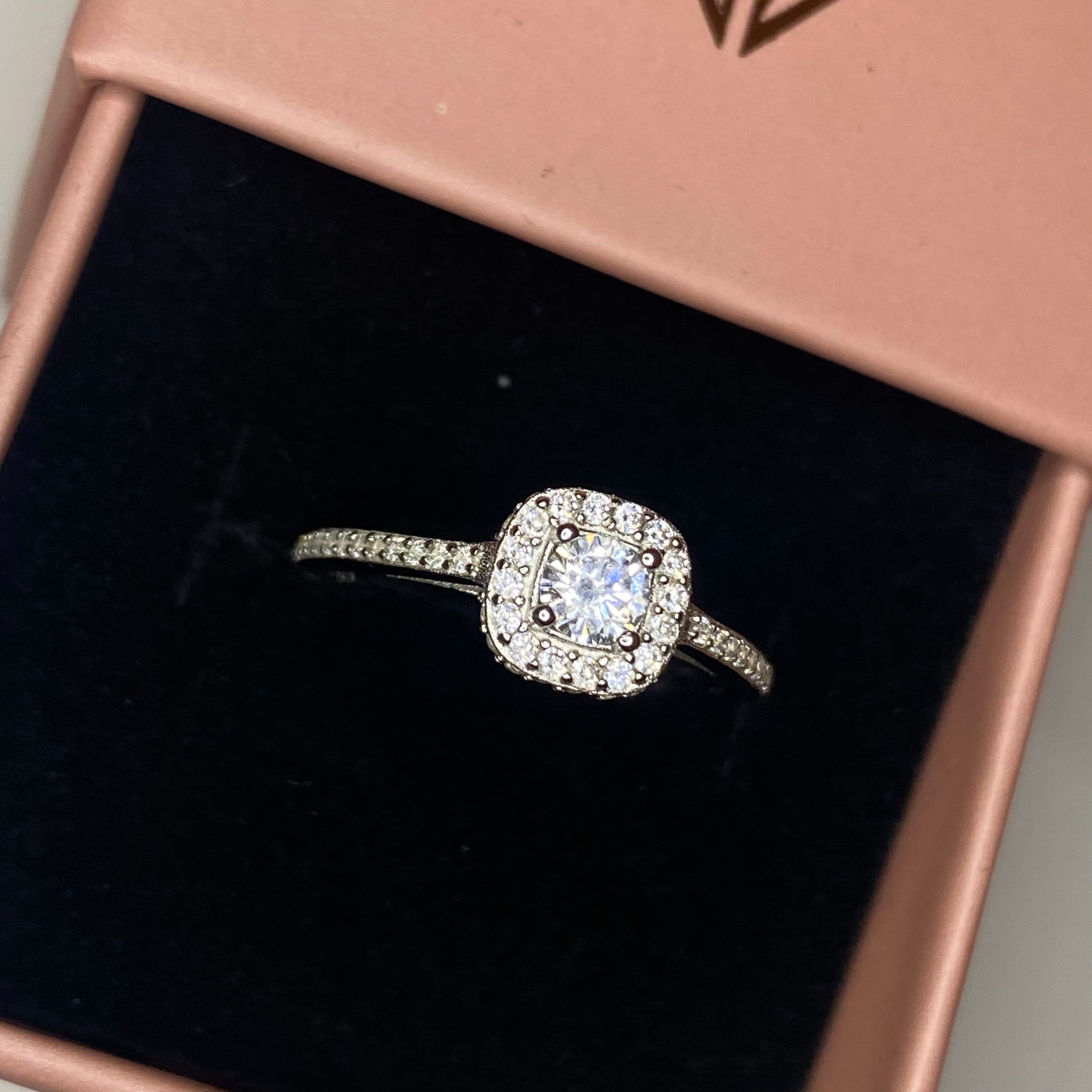 A silver square ring with a central cubic zirconia and surrounded by smaller clear stones on the band.