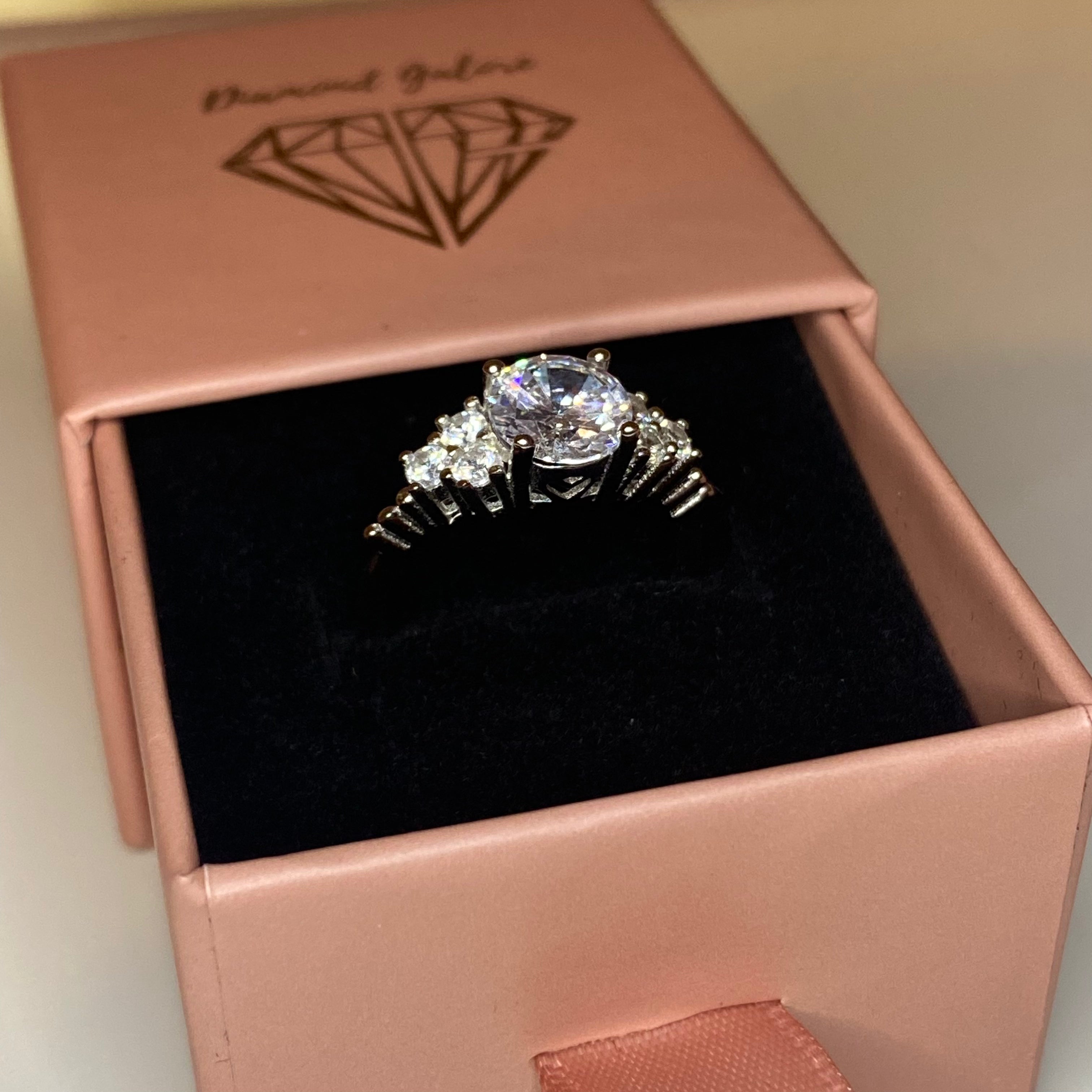 An elegant sterling silver ring with a large central clear cubic zirconia stone, surrounded by smaller clear stones, set in a silver-tone band.