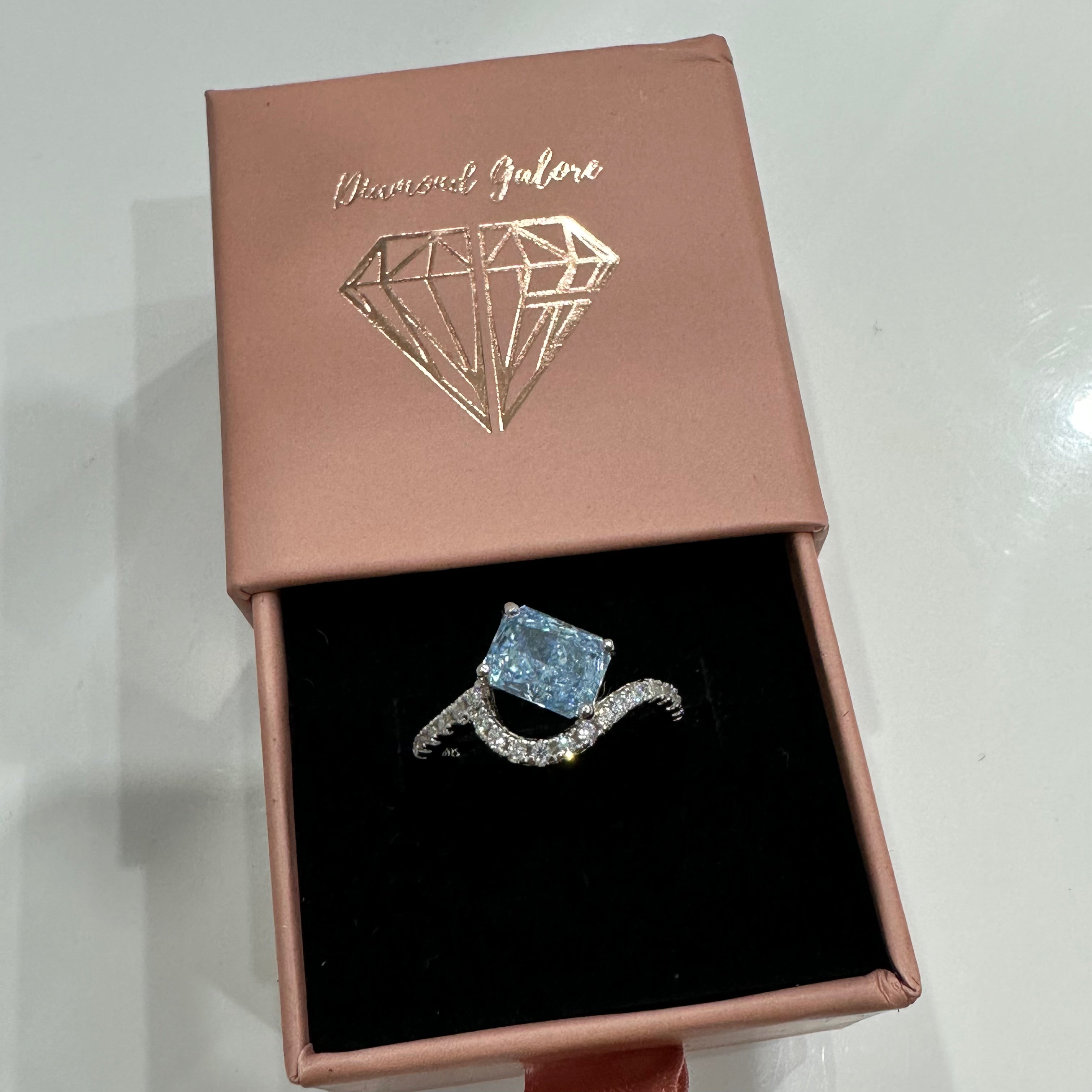 A sterling silver ring featuring a main stone (light-blue-color), shaped as a rectangle and set with smaller round diamonds.