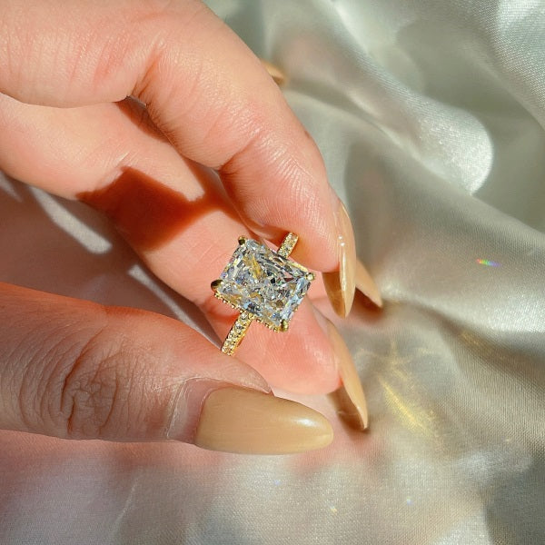 A gold-colored band engagement ring featuring a large rectangle-shaped central stone with smaller stones around it