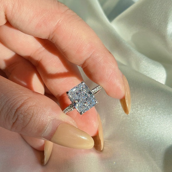 A silver-colored band engagement ring featuring a large rectangle-shaped central stone with smaller stones around it