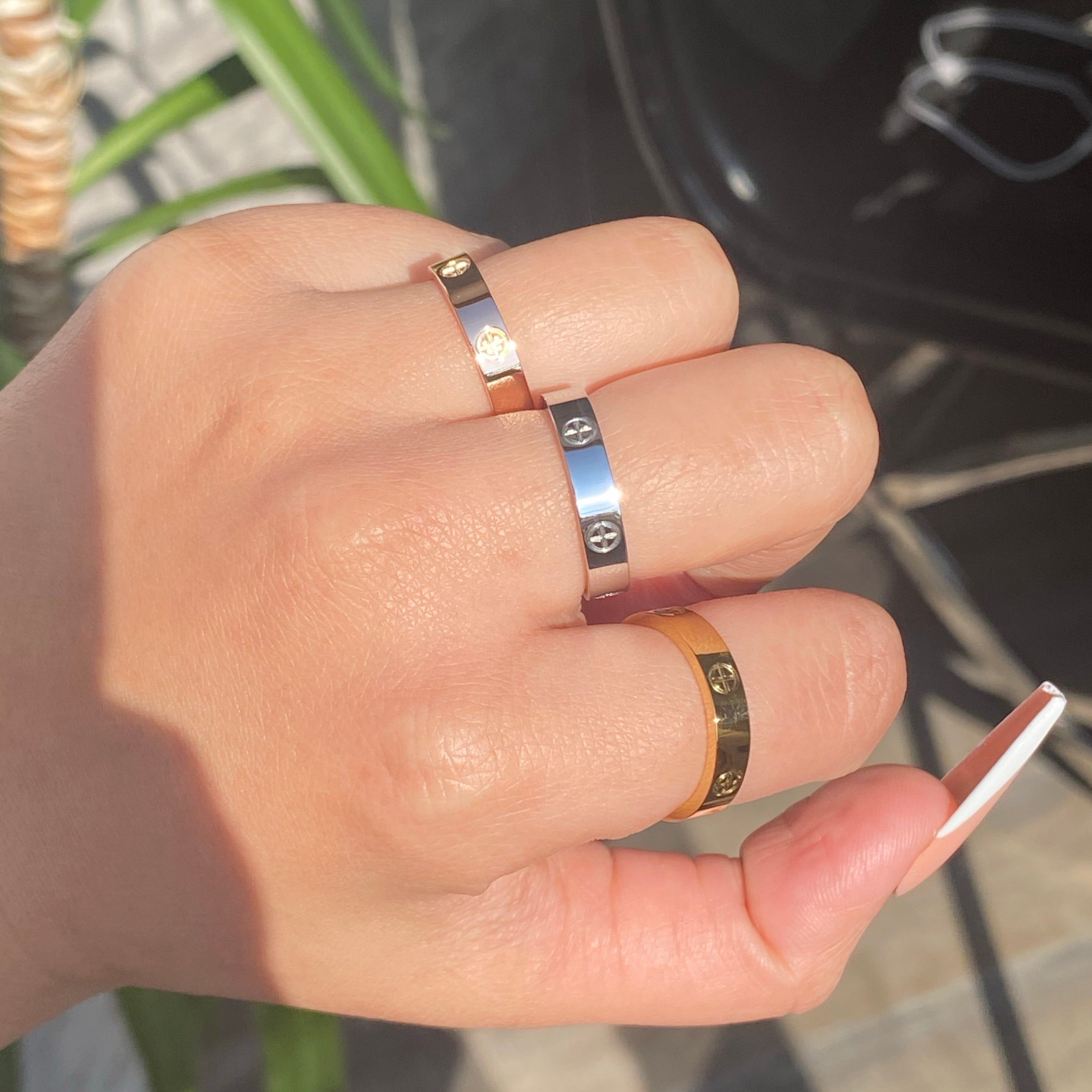 Three different-colored stainless steel rings with a plus design on women's hand with blurred background.