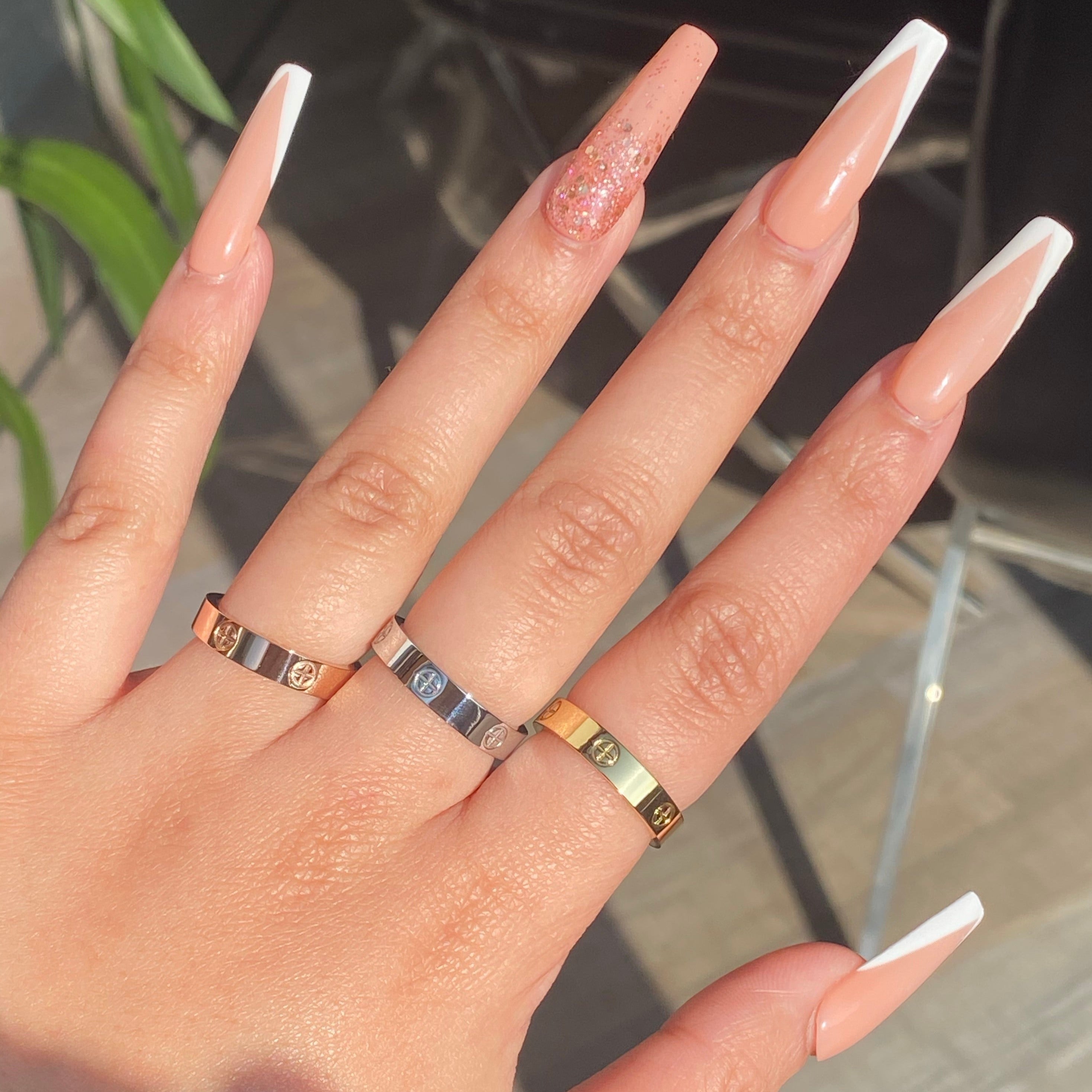 Three different-colored stainless steel rings with a plus design on women's hand with blurred background.
