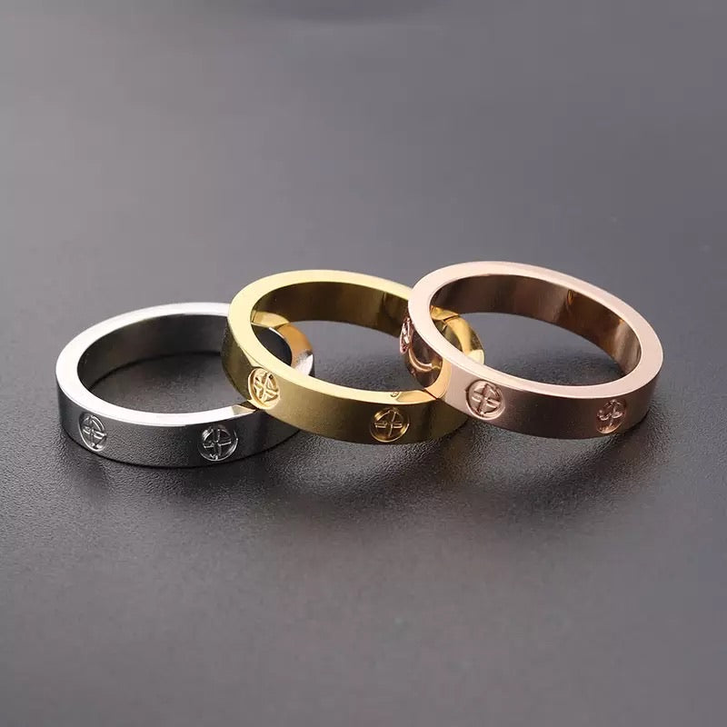 Three different-colored stainless steel rings with a plus design on grey background.