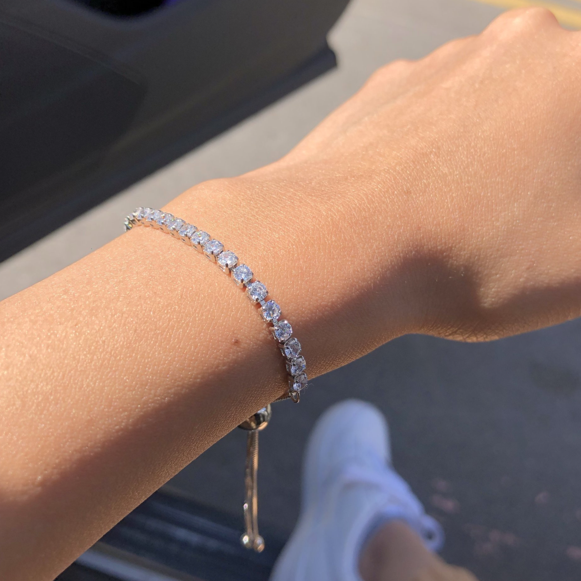 An adjustable silver bracelet with a row of sparkling stones, presented on a women's wrist.