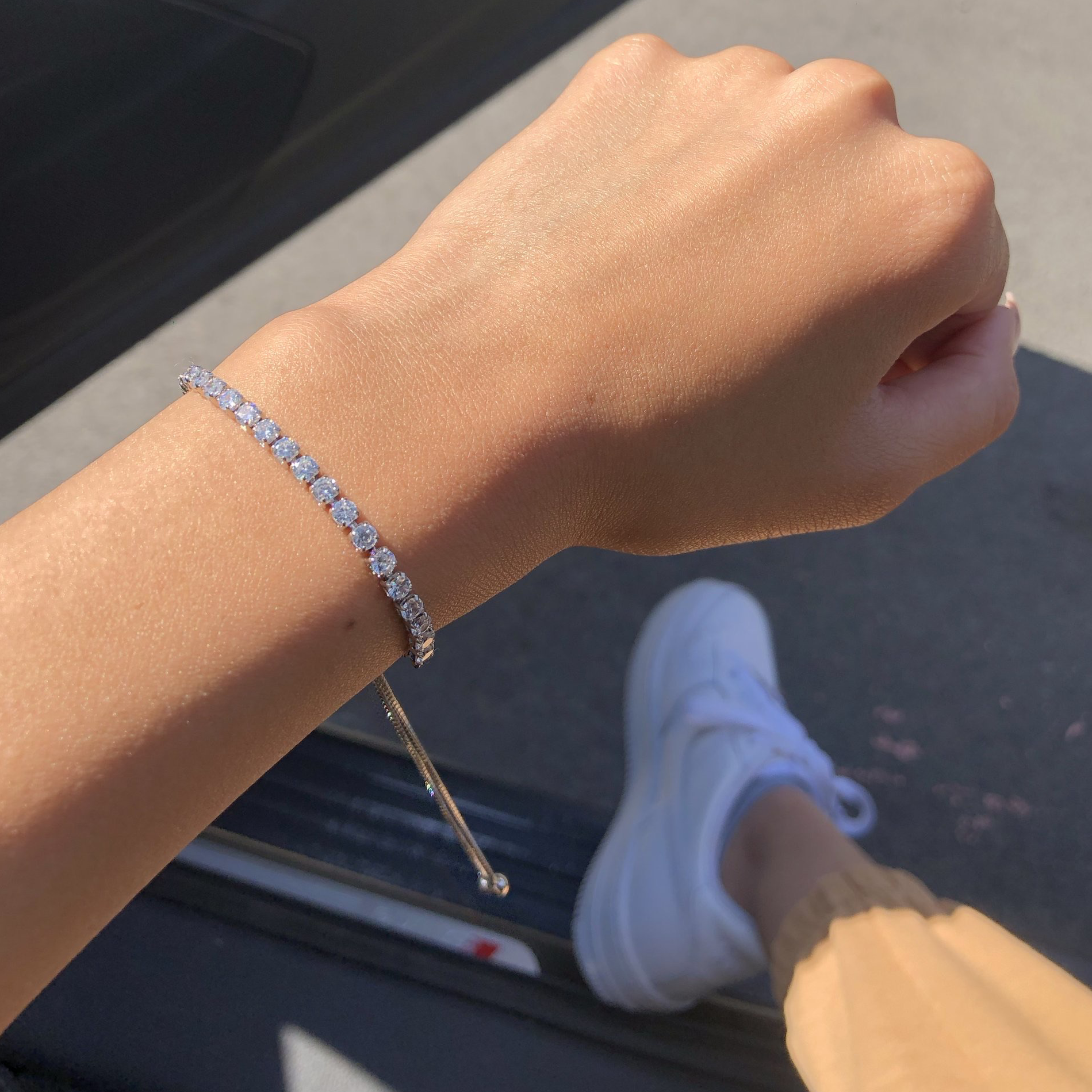 An adjustable silver bracelet with a row of sparkling stones, presented on a women's wrist.