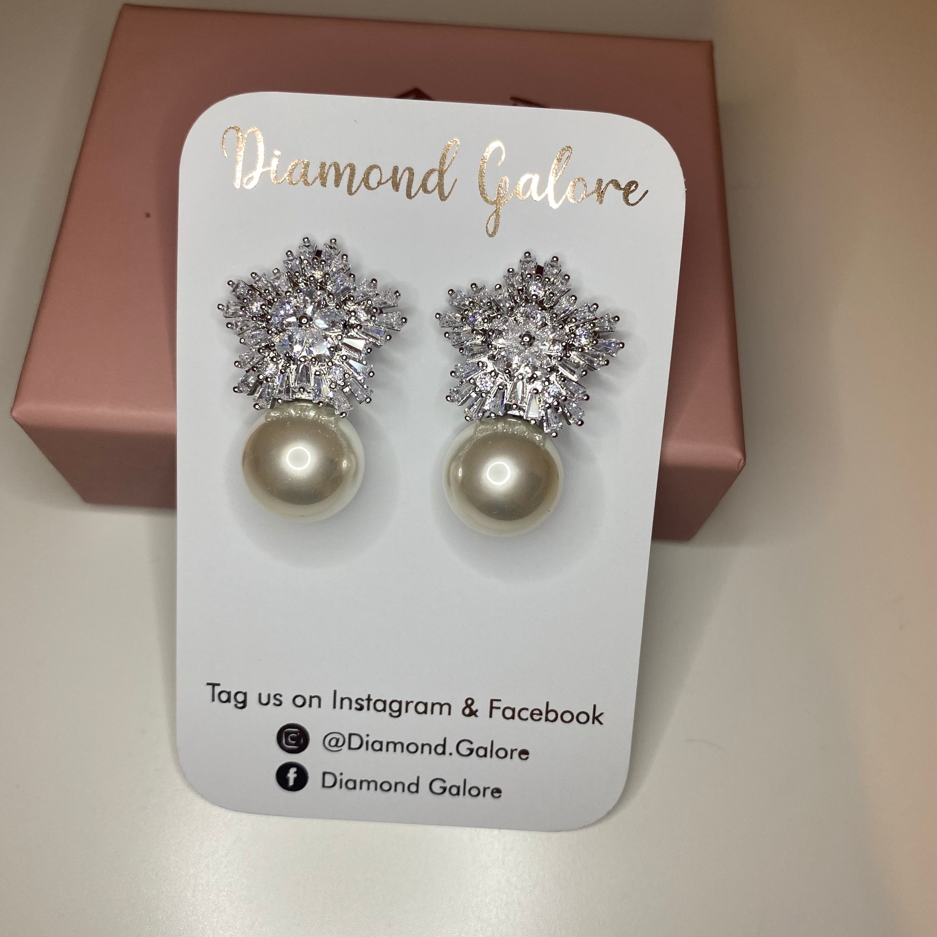 A pair of pearl earrings with raised texture and bullet-clutch back, likely silver or white gold, displayed on a brands card.