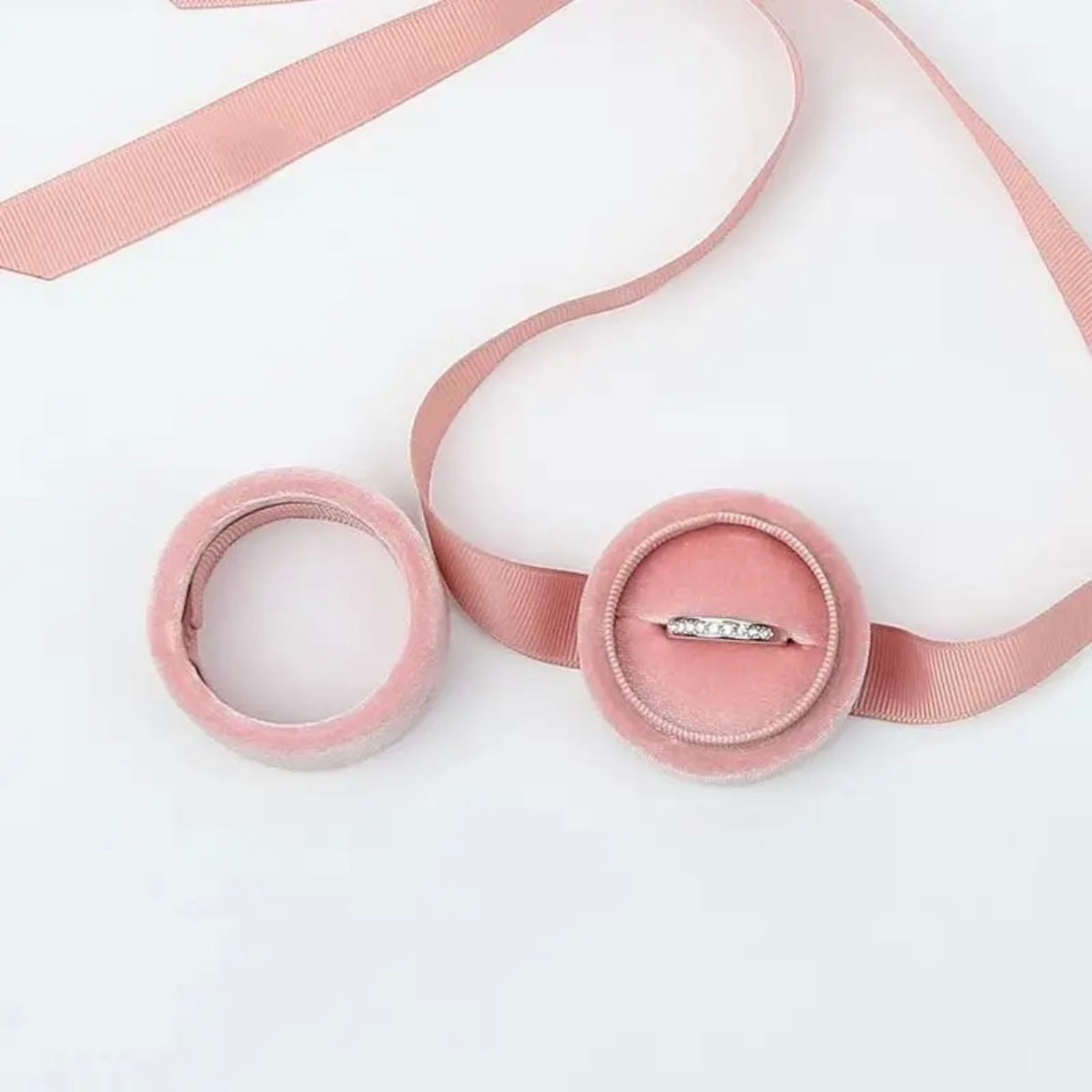A pink velvet gift box with a ribbon and a ring inside.
